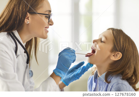 Pediatrician female doctor examining little boy patient's throat in medical clinic during checkup Pediatrician female doctor examining little boy patient's throat in medical clinic during checkup 127678160