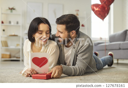 Happy Couple Unwrapping Gift With Red Heart For Valentine's Day At Home Happy Couple Unwrapping Gift With Red Heart For Valentine's Day At Home 127678161
