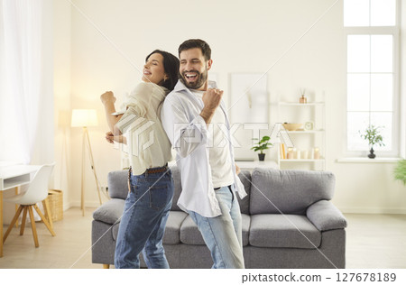 Smiling couple dancing together in cozy living room, celebrating and sharing happy moments together. 127678189