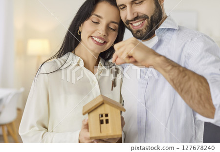 Happy smiling young family couple holding a toy house and the keys to their new home 127678240