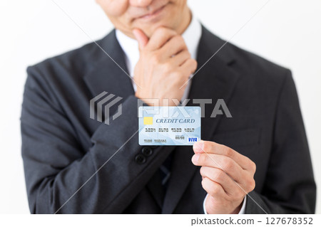 A businessman in a suit holding a credit card and worrying A businessman in a suit holding a credit card and worrying 127678352