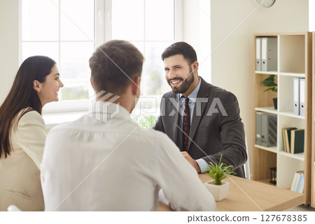 Business people talking with male colleague sitting at the desk in office on workplace. Business people talking with male colleague sitting at the desk in office on workplace. 127678385