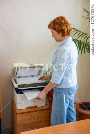 Woman copying documents using an office printer in a realistic administrative workspace. Paperwork routine, clerical tasks, and everyday office operations 127678576