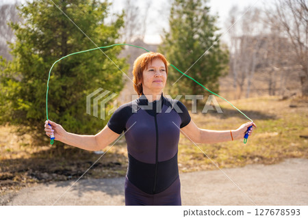 Woman jumping rope during morning workout in a green park. Cardio training, coordination, and energetic outdoor lifestyle. Woman jumping rope during morning workout in a green park. Cardio training, coordination, and energetic outdoor lifestyle. 127678593