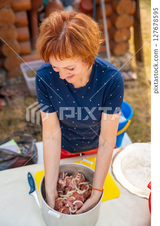 Woman mixing onions and meat with her hands in a bowl while preparing barbecue marinade. Homemade recipe, backyard food prep, and traditional grilling process. 127678595