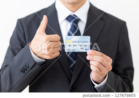 A businessman in a suit holding a credit card and giving a thumbs up A businessman in a suit holding a credit card and giving a thumbs up 127678605