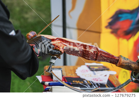 Chef slicing traditional Spanish jamon by hand with long knife at outdoor food festival booth. Concept of jamon, artisanal food, heritage based gourmet preparation. Spanish Culture and Food Festival 127679275