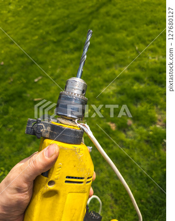 Damaged drill with electrical cord in grassy yard 127680127
