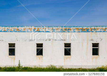 Weathered building with decayed Kyrgyzstani ornament and four windows in grassy area Weathered building with decayed Kyrgyzstani ornament and four windows in grassy area 127680150