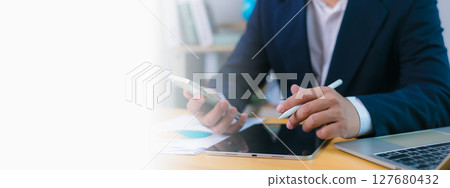 Businessman uses phone and a stylus on tablet at desk with a laptop and copy space , Modern remote work, digital productivity, technology integration, Efficient multitasking in a professional setting. Businessman uses phone and a stylus on tablet at desk with a laptop and copy space , Modern remote work, digital productivity, technology integration, Efficient multitasking in a professional setting. 127680432