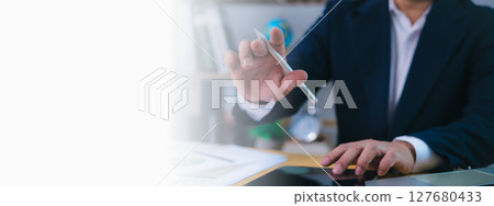 Businessman working at desk using a digital pen and tablet for data analysis, decision-making, business strategy, innovation, financial planning, productivity in a modern office with copy space. 127680433