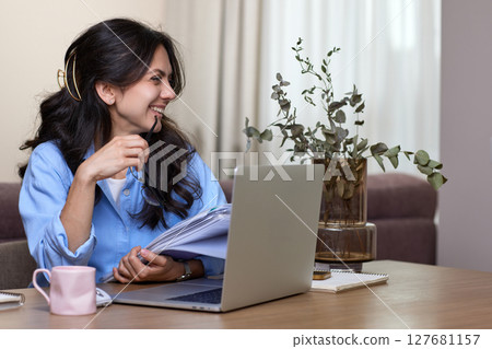 happy woman in blue shirt holds folders uses laptop in home office, copy space happy woman in blue shirt holds folders uses laptop in home office, copy space 127681157