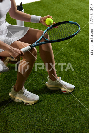 Tennis player sitting on grass with racket and ball ready for match preparation Tennis player sitting on grass with racket and ball ready for match preparation 127681349