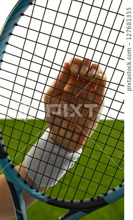 Hand holding tennis racket against grass court background Hand holding tennis racket against grass court background 127681355