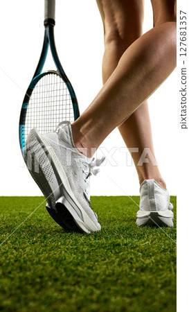 Tennis player legs and racket resting on grass court in athletic shoes against white background Tennis player legs and racket resting on grass court in athletic shoes against white background 127681357