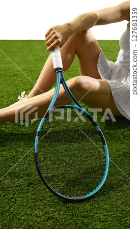 Tennis player relaxing on grass court holding racket with legs crossed in white sports attire 127681359