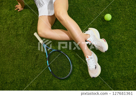 Tennis player resting on grass court with racket and tennis ball nearby Tennis player resting on grass court with racket and tennis ball nearby 127681361