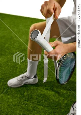 Tennis player preparing racket grip on grass court with focus on hands and equipment 127681369