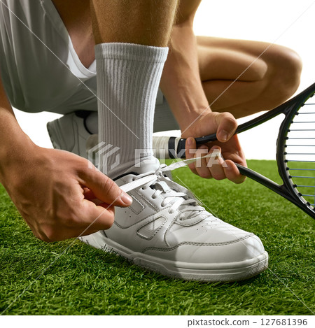 Tennis player tying sneakers on grass court holding racket preparing for match close up. Pre-match 127681396