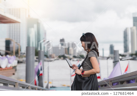 Happy young southeast asian woman teenager and blogger using smartphone searching for travel guide. world explorer Chao Phraya river Bangkok Asia with local cultural tourism experience concept 127681464