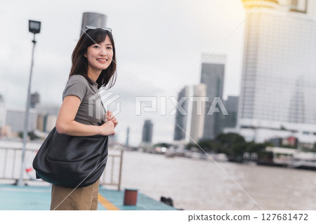 Happy solo southeast asian woman teenager blogger world travel explorer on local cultural tourism experience in Thailand wait for express boat on Chao Phraya river in Bangkok Asia travel concept 127681472