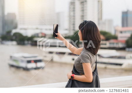 Solo southeast asian woman teenager blogger on world travel tourism. happy explorer take photo with smartphone of boat on Chao Phraya River. Local cultural experience in Bangkok Thailand Asia Solo southeast asian woman teenager blogger on world travel tourism. happy explorer take photo with smartphone of boat on Chao Phraya River. Local cultural experience in Bangkok Thailand Asia 127681481