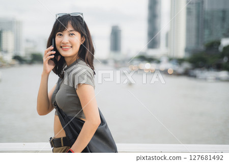 Happy solo Southeast Asian woman teenager blogger world travel tourism concept. Local cultural experience for explorer Bangkok Thailand. Wait for friend express joy by boat Chao Phraya River Asia 127681492