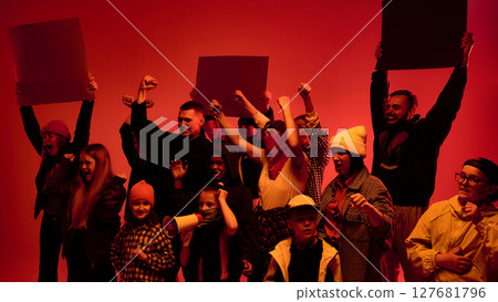 Group of diverse people holding protest signs with raised fists in red lighting, against deportation policy 127681796