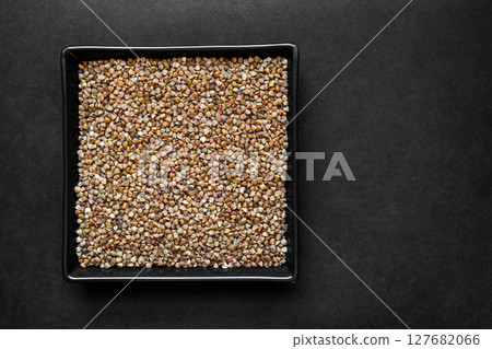 Buckwheat Grains in the Black Plate on Black Surface Background With Free Space Buckwheat Grains in the Black Plate on Black Surface Background With Free Space 127682066