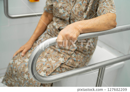 Asian elderly woman patient use toilet support rail in bathroom. 127682209