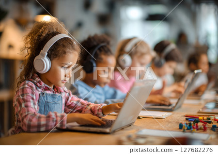 Children using notebooks with headphones during digital learning in classroom 127682276