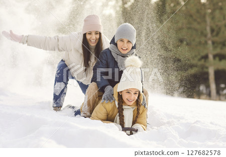 Happy smiling mother with two kids riding on snow slide in winter park. 127682578