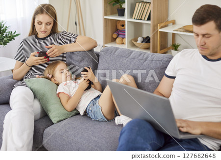 Family at home using laptop and smartphones sitting on sofa, entertaining online obsessed  127682648