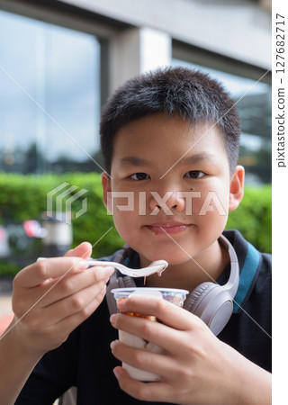Thai boy eating vanilla ice cream with chocolate syrup outdoors Thai boy eating vanilla ice cream with chocolate syrup outdoors 127682717
