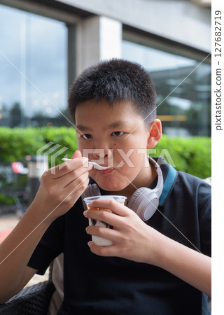 Thai boy eating vanilla ice cream with chocolate syrup outdoors 127682719