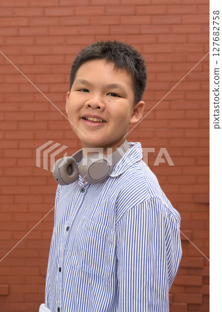 Thai boy in formal shirt with headphones posing against brick wall 127682758