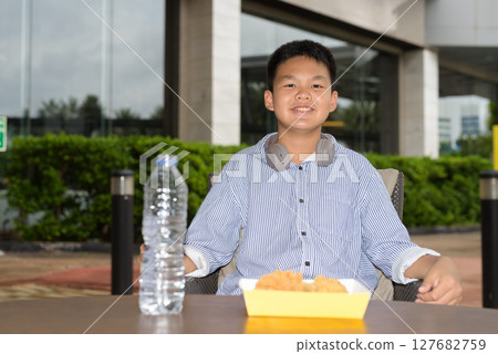 Thai boy eating fried chicken with headphones at outdoor table 127682759