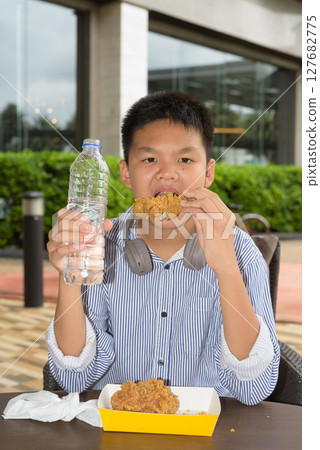 Thai boy eating fried chicken and drinking water outdoors Thai boy eating fried chicken and drinking water outdoors 127682775