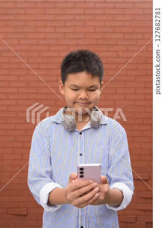 Thai boy in formal shirt with headphones posing against brick wall Thai boy in formal shirt with headphones posing against brick wall 127682781