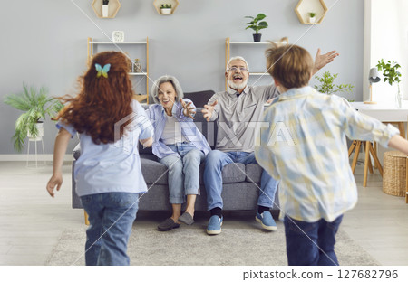 Grandchildren running to their senior happy smiling grandparent sitting on sofa at home to hug. Grandchildren running to their senior happy smiling grandparent sitting on sofa at home to hug. 127682796