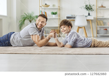 Father and son, dad happy playing with cute little son, compete arm wrestling on floor at home Father and son, dad happy playing with cute little son, compete arm wrestling on floor at home 127682860