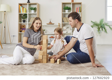 Happy parents playing educational game with daughter, building tower with wooden blocks together. 127682920