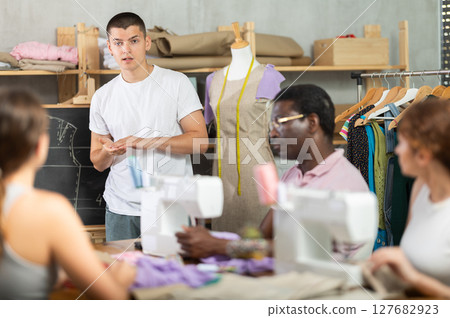 Young sewing instructor guiding adult beginners during practical workshop 127682923