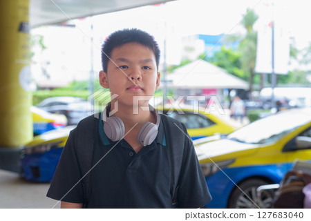 Thai teen boy wearing headphones with city taxis in background 127683040