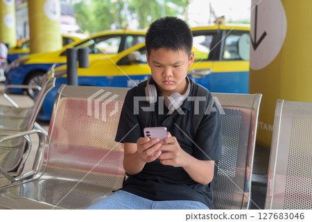 Thai teen boy wearing headphones using phone with city taxis in background 127683046