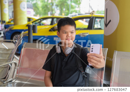 Thai teen boy wearing headphones using phone with city taxis in background 127683047