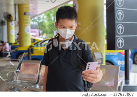 Thai boy with facial mask with taxis in background wearing headphones Thai boy with facial mask with taxis in background wearing headphones 127683062
