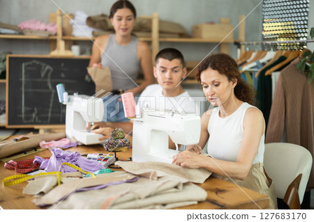 Middle-aged woman sewing while others working with sewing-machine and making details 127683170