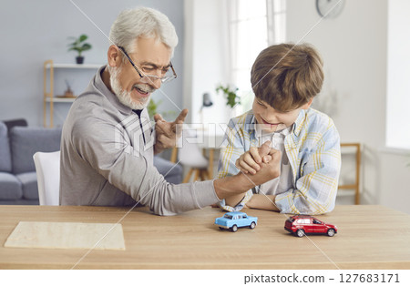 Senior grandfather arm wrestling with little boy grandson sitting at table in living room at home 127683171