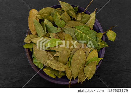 Dried up Bay Leaves Placed in Purple Plate on Black Stone Surface Background Dried up Bay Leaves Placed in Purple Plate on Black Stone Surface Background 127683179
